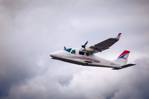 Light small plane flies against the background of white rainy clouds not high above the ground. Light aircraft on the air. A small tourist plane on an isolated white rainy clouds.