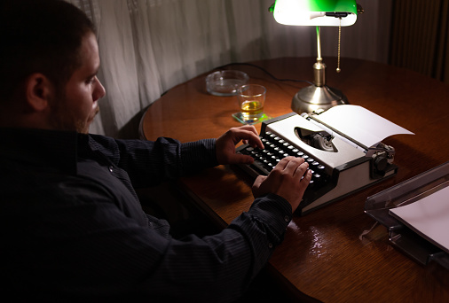 Young Writer sitting in his room at his house writing a story on his old typewriter.