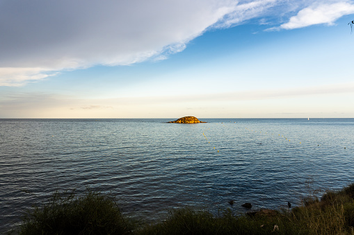 Small island in the sea at sunset, with cloudy sky