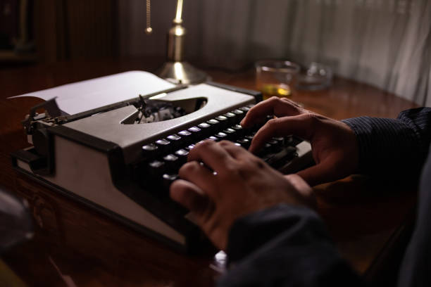 jeune écrivain assis dans sa chambre chez lui écrivant une histoire sur sa vieille machine à écrire en pensant où devrait aller l’histoire quoi écrire ensuite et en vérifiant son texte et son écriture. - typewriter typebar retro revival old photos et images de collection