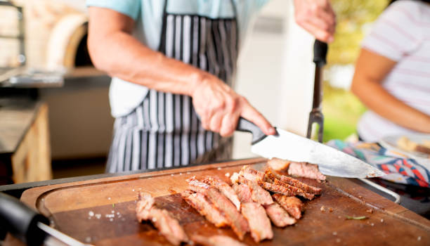 Man cutting freshly cooked steak during a summer barbecue Close-up of a man slicing up freshly cooked steak on a cutting board during a barbecue brazilian bbq stock pictures, royalty-free photos & images