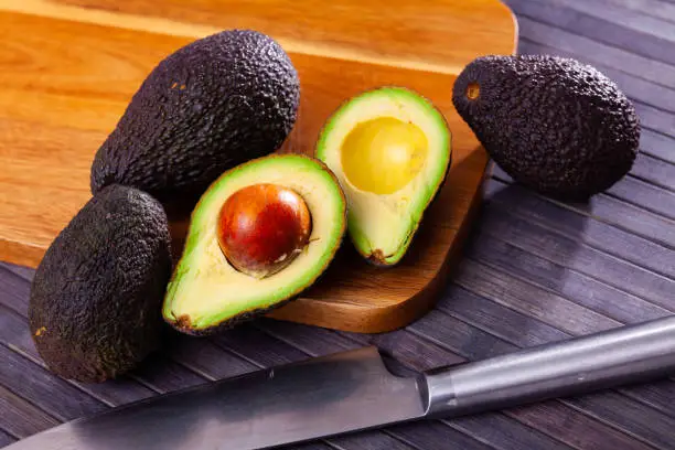 Photo of Whole and halved fresh avocados on wooden surface