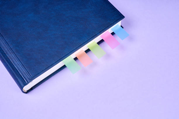 An office notepad with colorful sticky page markers sandwiched between pages on purple background