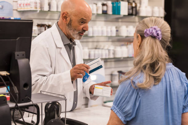 Mature pharmacist compares over-the-counter medications for female customer The mature adult male pharmacist compares two over-the-counter medications for the unrecognizable senior female customer. over-the-counter medications stock pictures, royalty-free photos & images