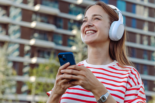 Cheerful young woman using smart phone, headphones and smiling.