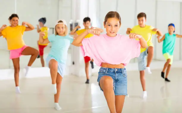 Photo of Preteen girl practicing hip-hop movements during group dance lesson