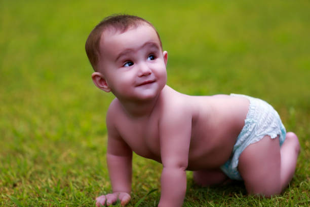 Cute baby child crawling on the grass wearing dry diaper during summer season wearing diaper.