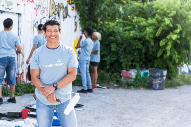 istock Male volunteer holds paint roller and smiles for camera 1419122326