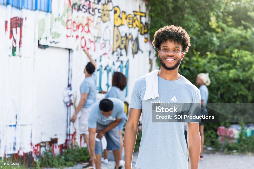 Others continue painting over graffiti, as student smiles for camera As the other volunteers continue painting over the graffiti, the young adult male college student smiles for the camera. 18-19 Years Stock Photo