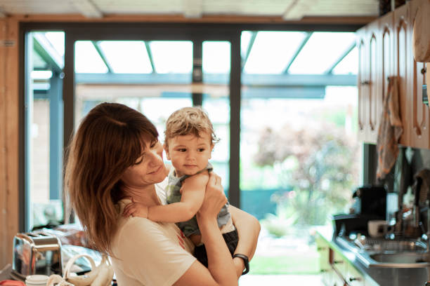 Young mother holding baby son in the kitchen. stock photo