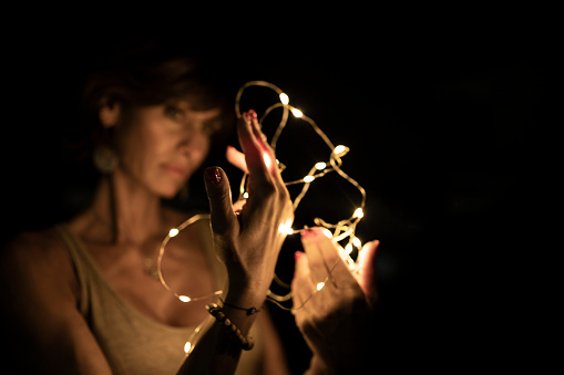Beautiful caucasian woman, blurred face, holding string lights in the dark. Copy space. Holidays or magic background or wallpaper.