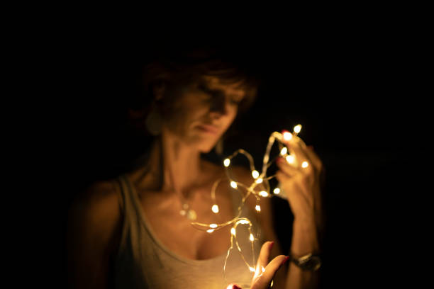 istock Woman, blurred face, holding string lights in the dark. Copy space. 1419125076