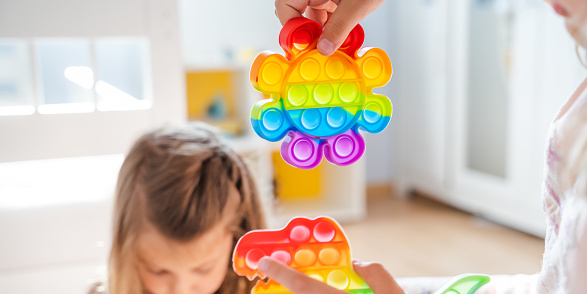 Little girls,kids,sisters play with colorful pop it children room,bedroom.Funny trendy silicone antistress colorful sensory push toy popit.Flapping fidget.Rainbow color.Cure of autism.Stress reliever.