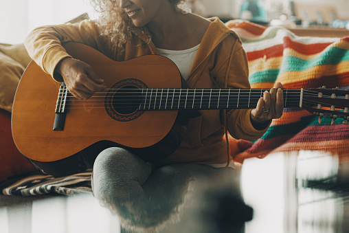 One woman at home playing guitar and having fun alone in relax leisure activity. People play music instrument and learn new activity. Female in indoor hobby using acoustic guitar and smiling happy