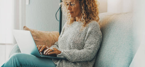 istock Horizontal banner image with young mature woman using laptop sitting on the sofa. Concept of surfing the web people. Modern female working on computer at home in relax time. Lady use notebook happy 1419130638