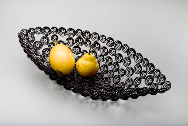 Pear and a passion fruit inside a canoe shaped black metal fruit bowl, with spirals cut outs, isolated on white