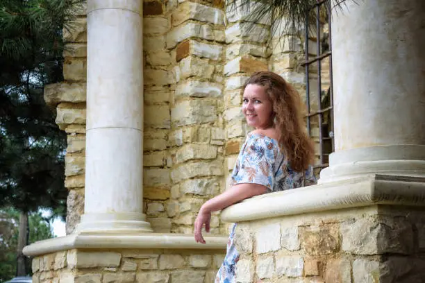 Photo of Portrait of young pretty woman on stairs near ancient historical building from stone and seashells