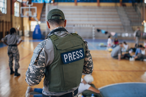 Diverse group of people, soldiers on humanitarian aid to civilians in school gymnasium, after natural disaster happened in city. Army press is also with the people.