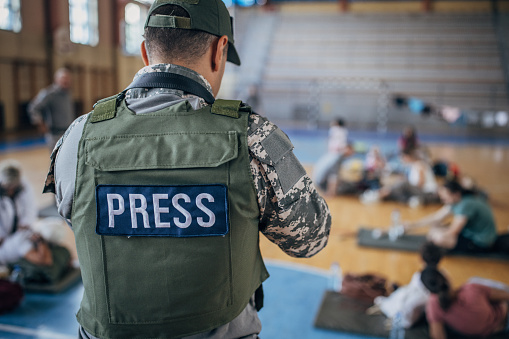 Diverse group of people, soldiers on humanitarian aid to civilians in school gymnasium, after natural disaster happened in city. Army press is also with the people.