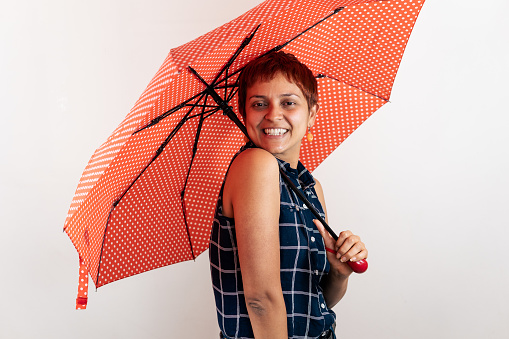 a mid age Latin woman holds an umbrella while looking at the camera