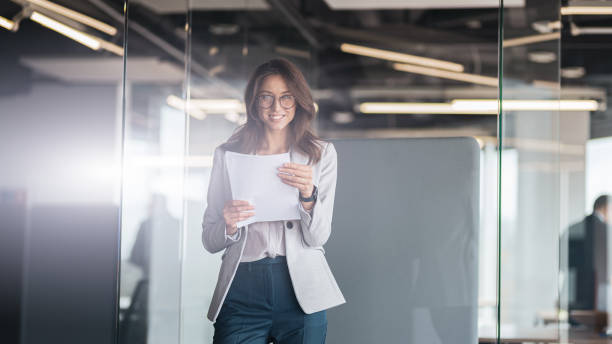 istock Young smiling businesswoman with documents standing at office and look at camera 1419137516