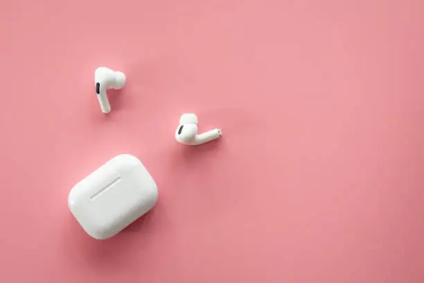 Wireless in-ear headphones with a case on a pink background, flat lay, conceptual minimalism.