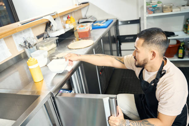Asian guy in apron preparing his kitchen for a cook-off Talented chef taking ingredients out of the fridge while working in the restaurant kitchen busy restaurant tables stock pictures, royalty-free photos & images