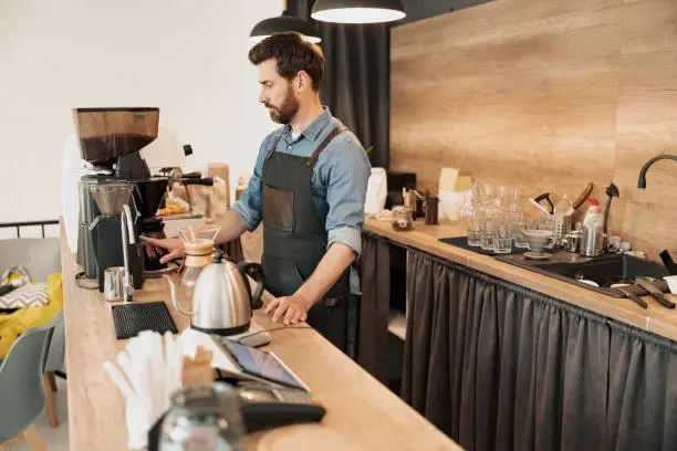 Handsome barista wearing apron grinds coffee beans in coffeemachine