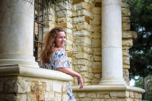 Photo of Portrait of young pretty woman on stairs near ancient historical building from stone and seashells