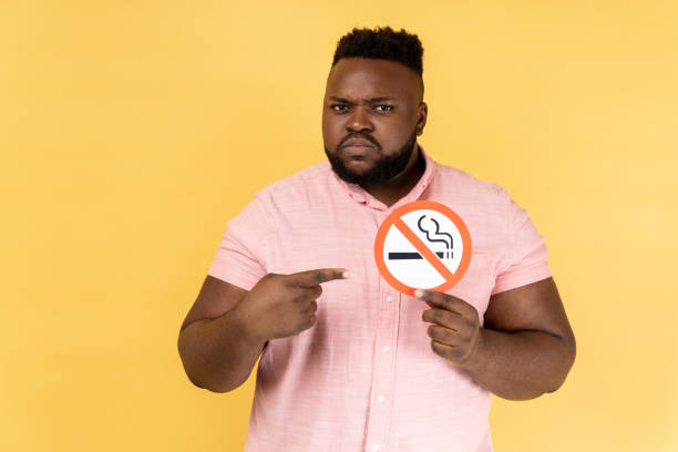 hombre serio sosteniendo y señalando con el dedo a la señal de no fumar en las manos, dejar de fumar, no fumar día. - african descent addiction african ethnicity rudeness fotografías e imágenes de stock