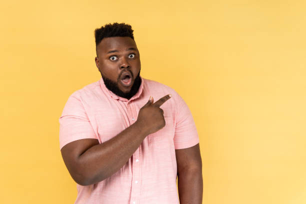 asombrado sorprendido hombre vestido con camisa rosa señalando a un lado con el dedo, mostrando el área de publicidad. - shock absorber fotografías e imágenes de stock