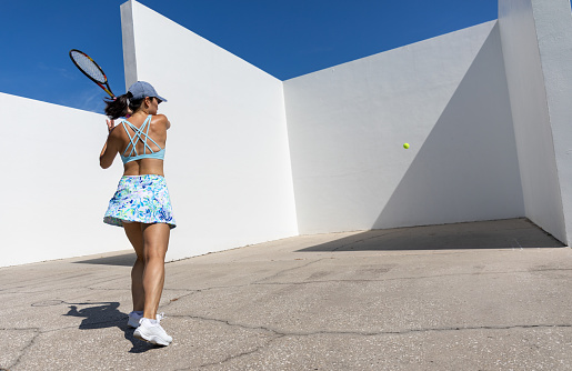 Young Korean woman tennis player practicing big open stance  forehand against the wall of a handball court.