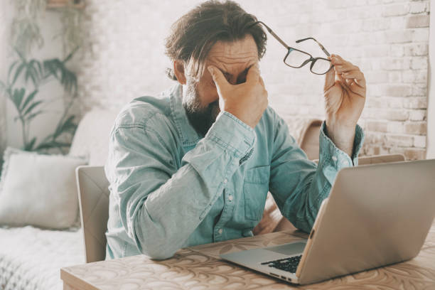 istock Tired man holding glass and touching is eyes after over work on notebook computer. Online activity and problems to solve concept. Modern worker people using laptop at table desk. Economy difficulty 1419143976