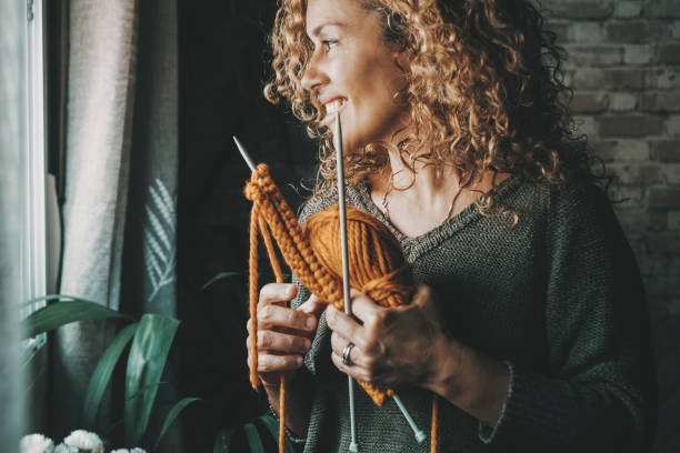 Side portrait of woman smiling and enjoying knit wool work at home alone. Middle age lady in knitting leisure hobby activity. People and time in the house. Concept of single lifestyle happy female stock photo