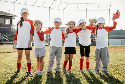 Team of elementary age children playing little league baseball in local park. Boys and Girls are wearing matching sports uniforms and using baseball gear