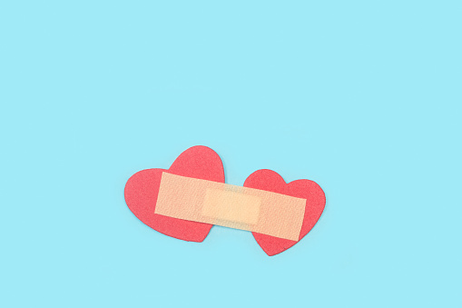 An adhesive bandage uniting two red paper hearts on a light blue background with copy space