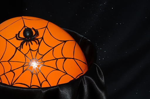 Halloween decor - black spider and cobwebs on a solid orange background. On a black background, place for text.