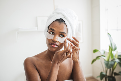 Young woman applying eye mask on her face in the bathroom at home