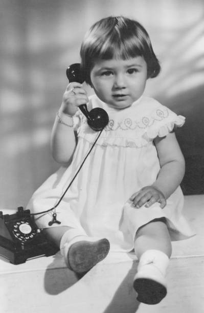 schwarz-weiß-bild aus den späten fünfziger jahren, ein kleines mädchen, das mit einem telefon posiert und in die kamera schaut - 1950 1959 stock-fotos und bilder