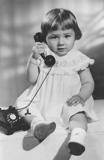 Imagen en blanco y negro tomada a finales de los años cincuenta, niña posando sosteniendo un teléfono mirando a la cámara photo
