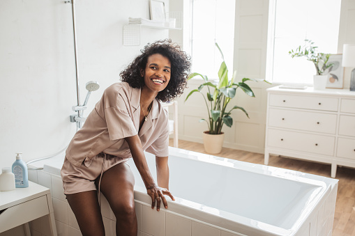 Young woman preparing bathtub full of bubbles for her spa day at home.