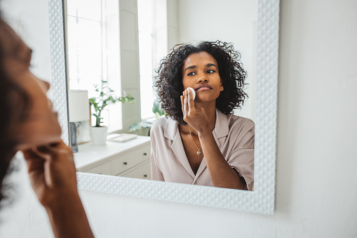 Attractive young woman cleaning her face with a cotton pad in the bathroom at home