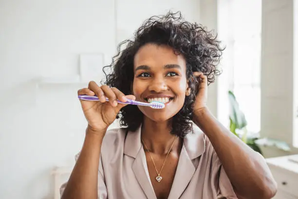 Photo of Smiling woman brushing healthy teeth in bathroom