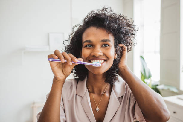 smiling woman brushing healthy teeth in bathroom - brushing teeth women toothbrush brushing imagens e fotografias de stock