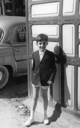 Black and White Vintage image taken in the 60s, little boy looking at the camera full length wearing a blazer and shorts , 1960