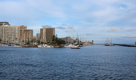 Looking at the Waikiki Yacht Club from across the Ala Wai channel against a blue cloud sky and Diamond Head in the background.  Several hotel and condominium buildings in the background.