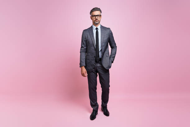 istock Confident mature man in full suit looking at camera while standing against pink background 1419155201