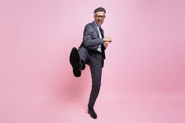 istock Furious mature man in formalwear throwing leg kick while standing against pink background 1419155237