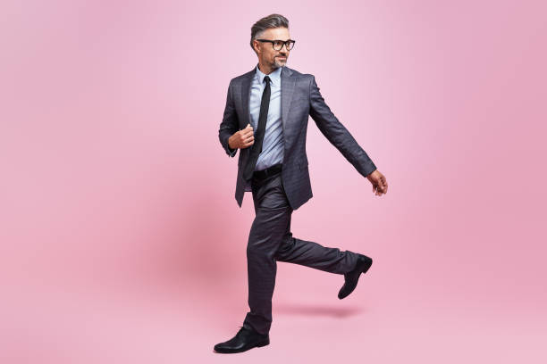 Confident mature man in full suit walking against pink background