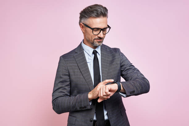 istock Confident mature man in formalwear checking the time while standing against pink background 1419156219